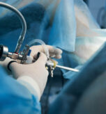 Close up photo of a medical worker in latex gloves standing with a hysteroscope near the patient